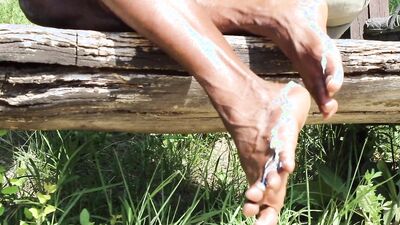 Kinky black guy rubs oil on his feet and teases outdoors