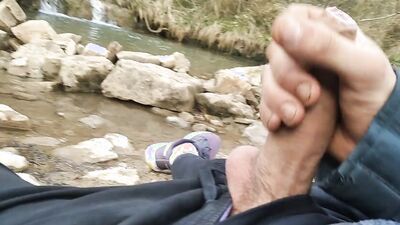 Horny lad is sitting by the creek while stroking his hard cock