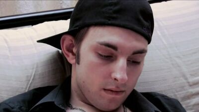 A dude in a baseball cap undresses and jerks off on the couch