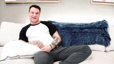 Tattooed man strips naked and grabs his cock to stroke it